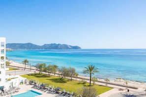 A coastal hotel with a swimming pool, lounge chairs, and a view of the sea and mountains. - Seafront Apartment in Cala Millor – Mallorca (Cala Millor)