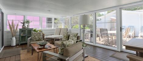 A sunlit room with a sofa, coffee table, and a dining area with chairs and a table.