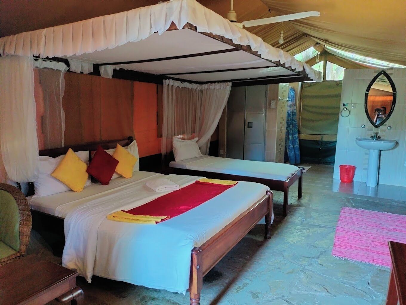 Une chambre avec deux lits, dont un lit à baldaquin, un plancher en bois, un miroir et un lavabo.