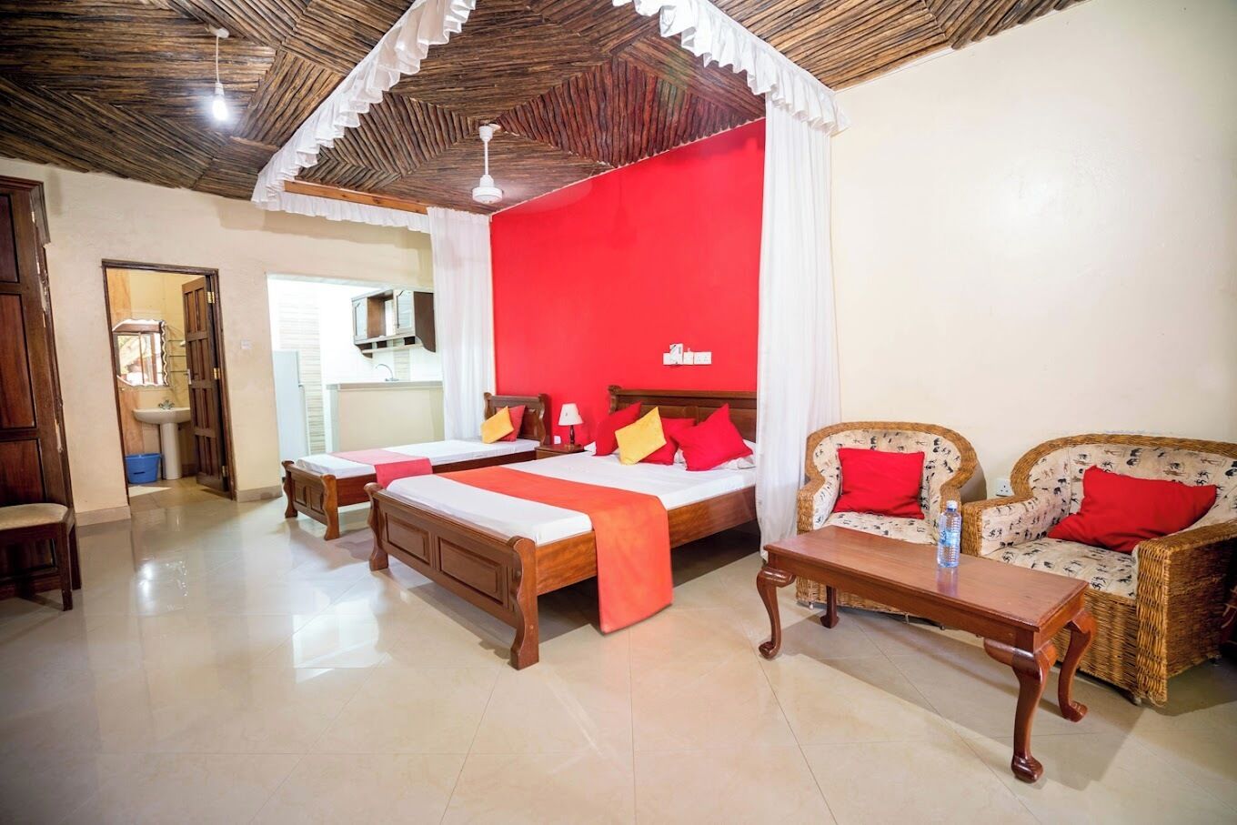 A hotel room with two wooden beds, a red accent wall, a wicker sofa, and a wooden coffee table.