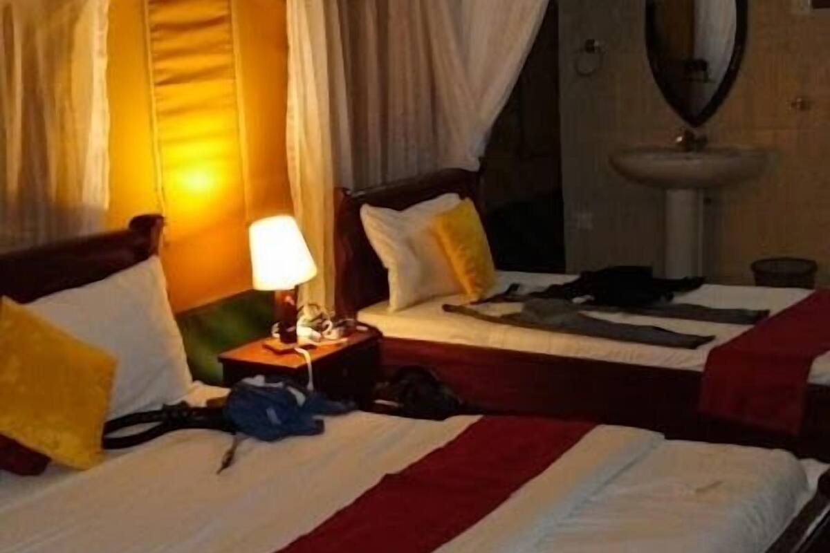 A tent-style room with two beds, each with white bedding and red accents. There is a bedside table with a lamp and a small table with a yellow object.