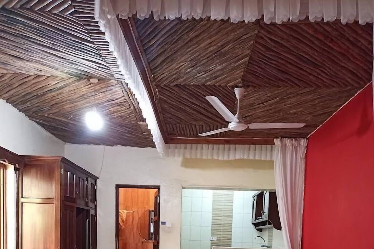 A room with two beds, a ceiling fan, a wooden wardrobe, and a bathroom visible through an open door.