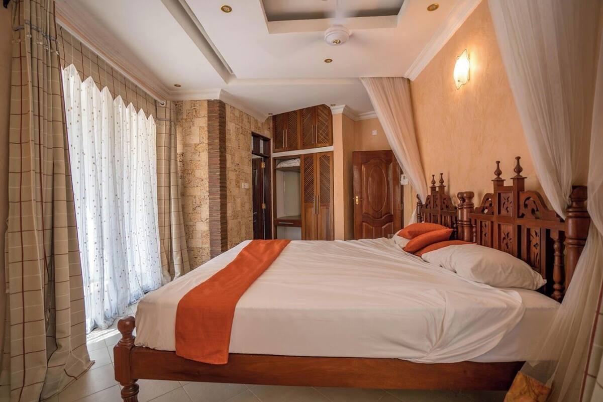 A bedroom with a large bed, wooden headboard, and a window with curtains.