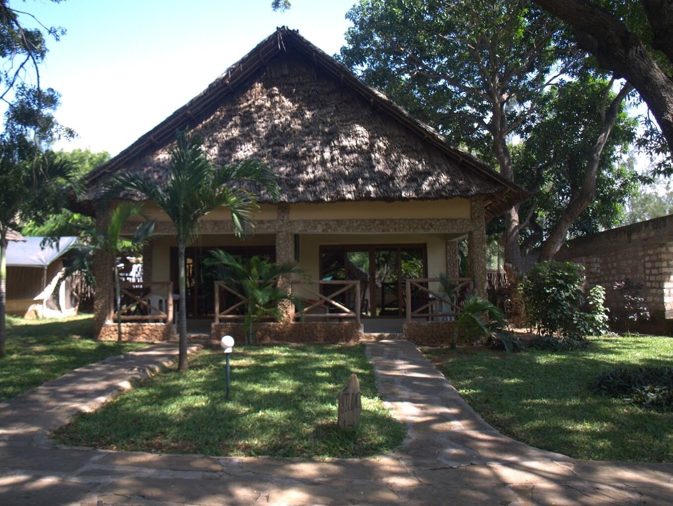 A thatched-roof structure with a stone base, surrounded by greenery and a paved pathway.