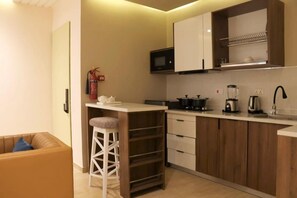 A compact kitchen with a microwave, stove, and coffee maker. There is a white bar stool and a fire extinguisher on the wall. - Vievely Suites and Apartments (Lagos)