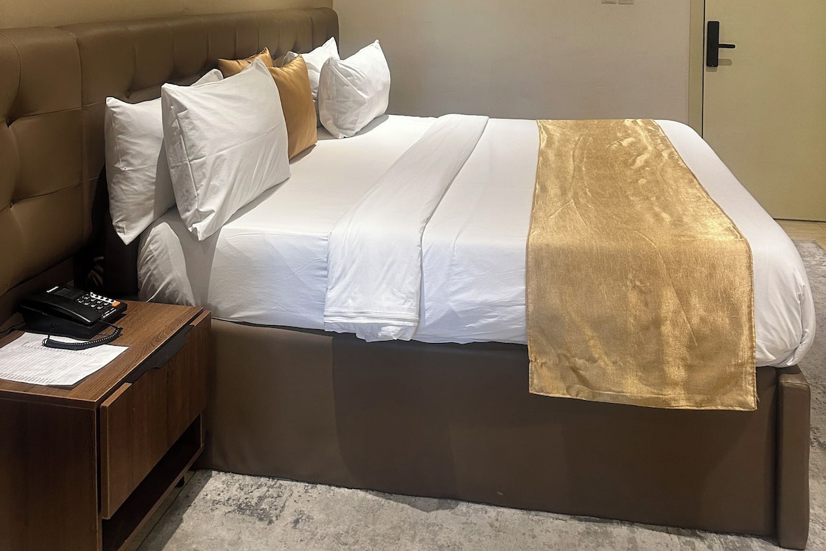 Una habitación de hotel con cama, mesita de noche y aire acondicionado.