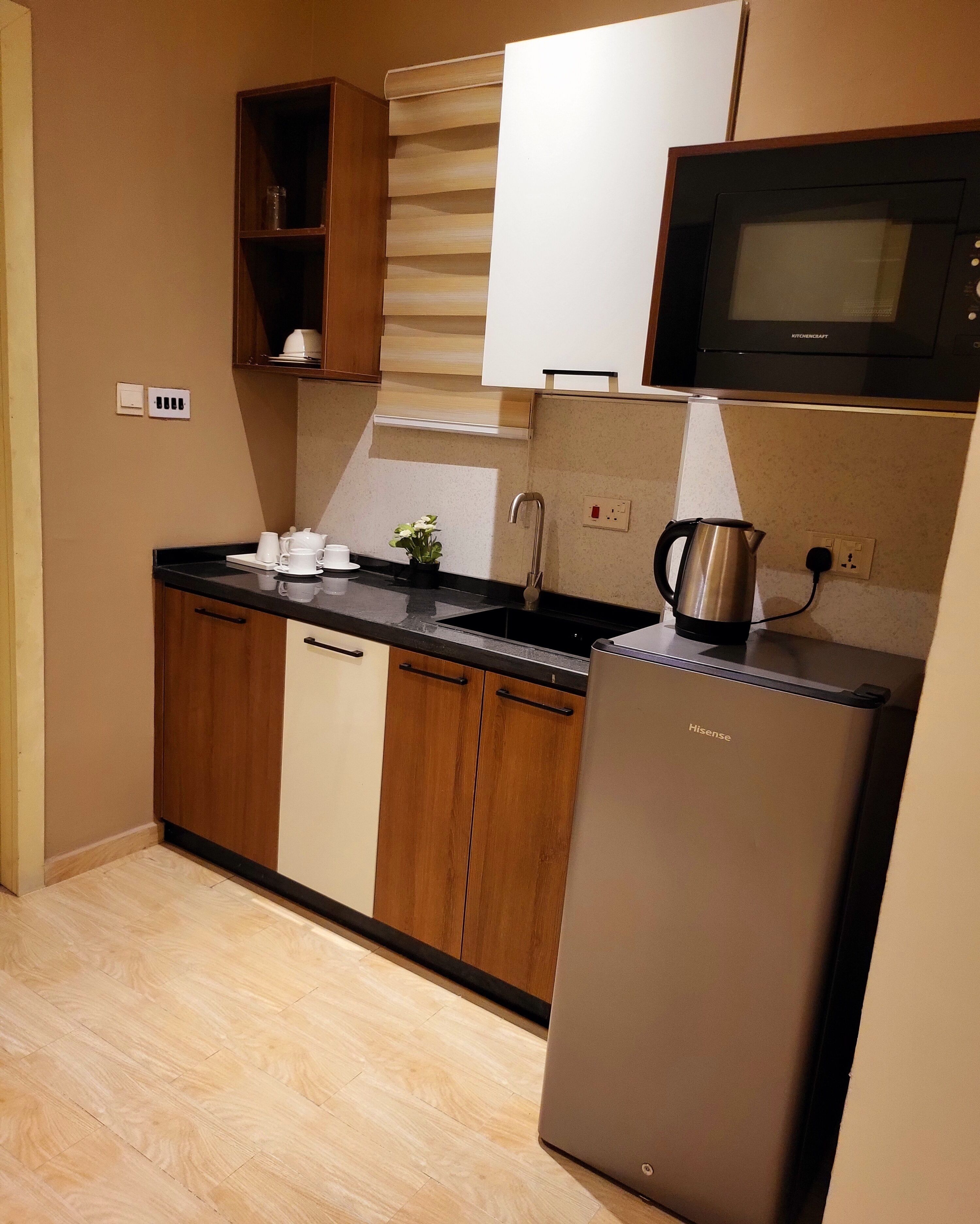 A modern kitchen with wooden cabinets, a stainless steel refrigerator, a microwave, and a kettle.