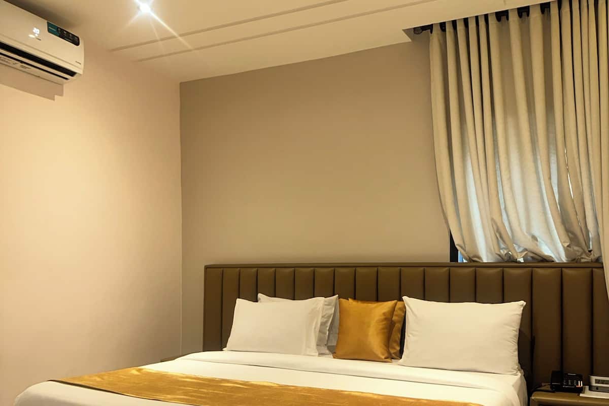 Una habitación de hotel con cama, mesita de noche y equipo de aire acondicionado.