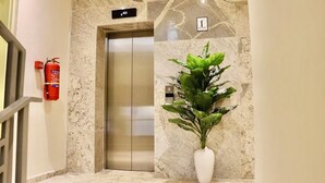 A marble-floored hallway with an elevator marked "1 FLOOR" and a potted plant. - Vievely Suites and Apartments (Lagos)