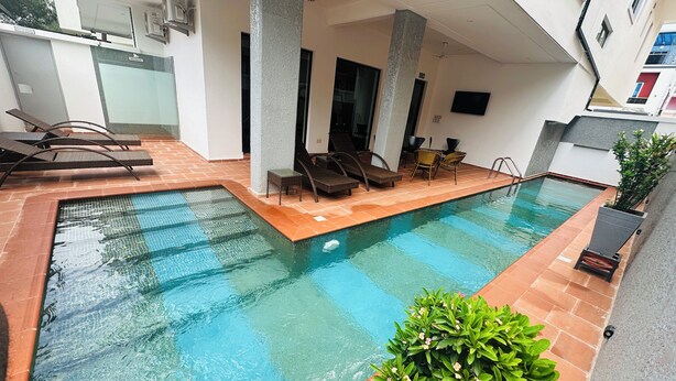 A swimming pool with lounge chairs and a small table, surrounded by a tiled patio area. - Vievely Suites and Apartments (Lagos)