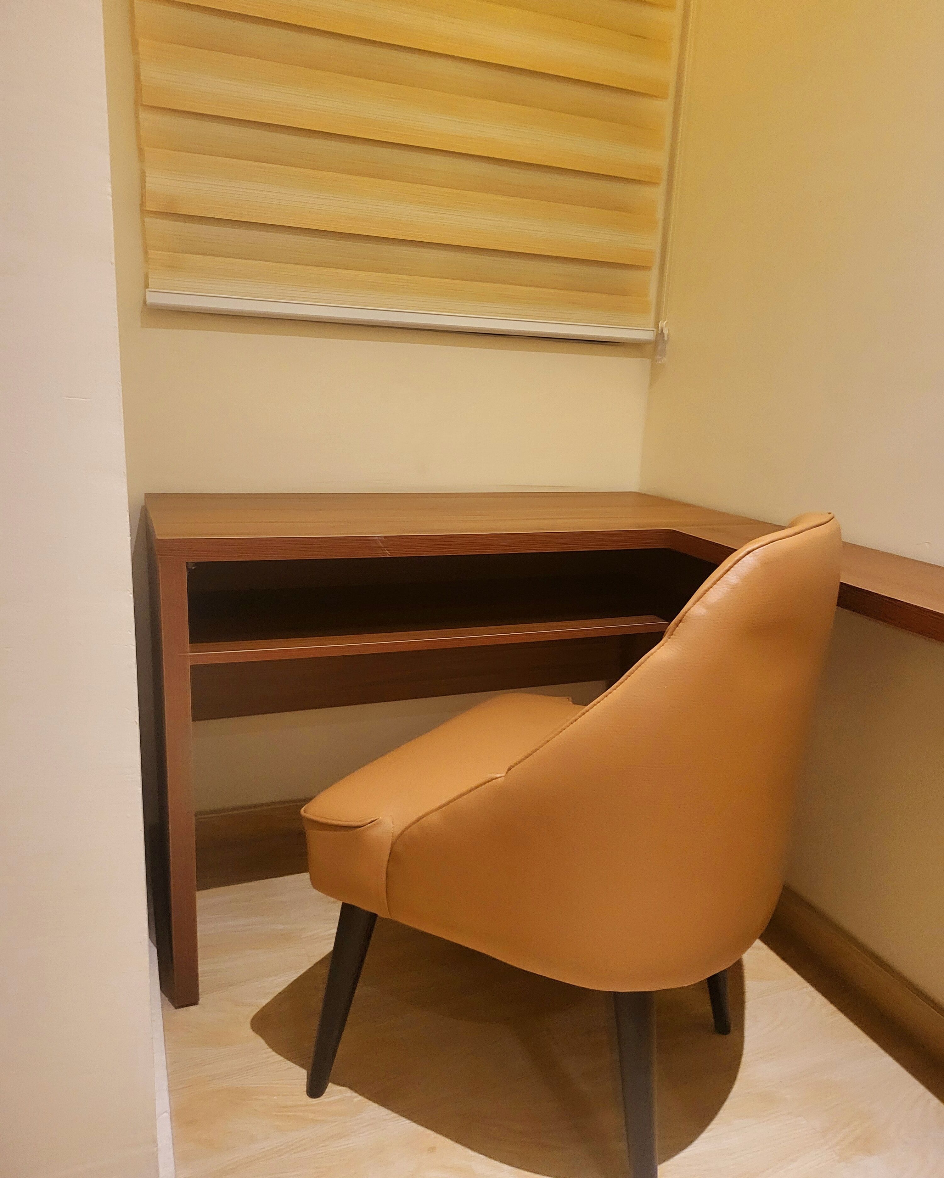 Un bureau d’angle avec un fauteuil en cuir, un bureau en bois et une fenêtre avec des stores.
