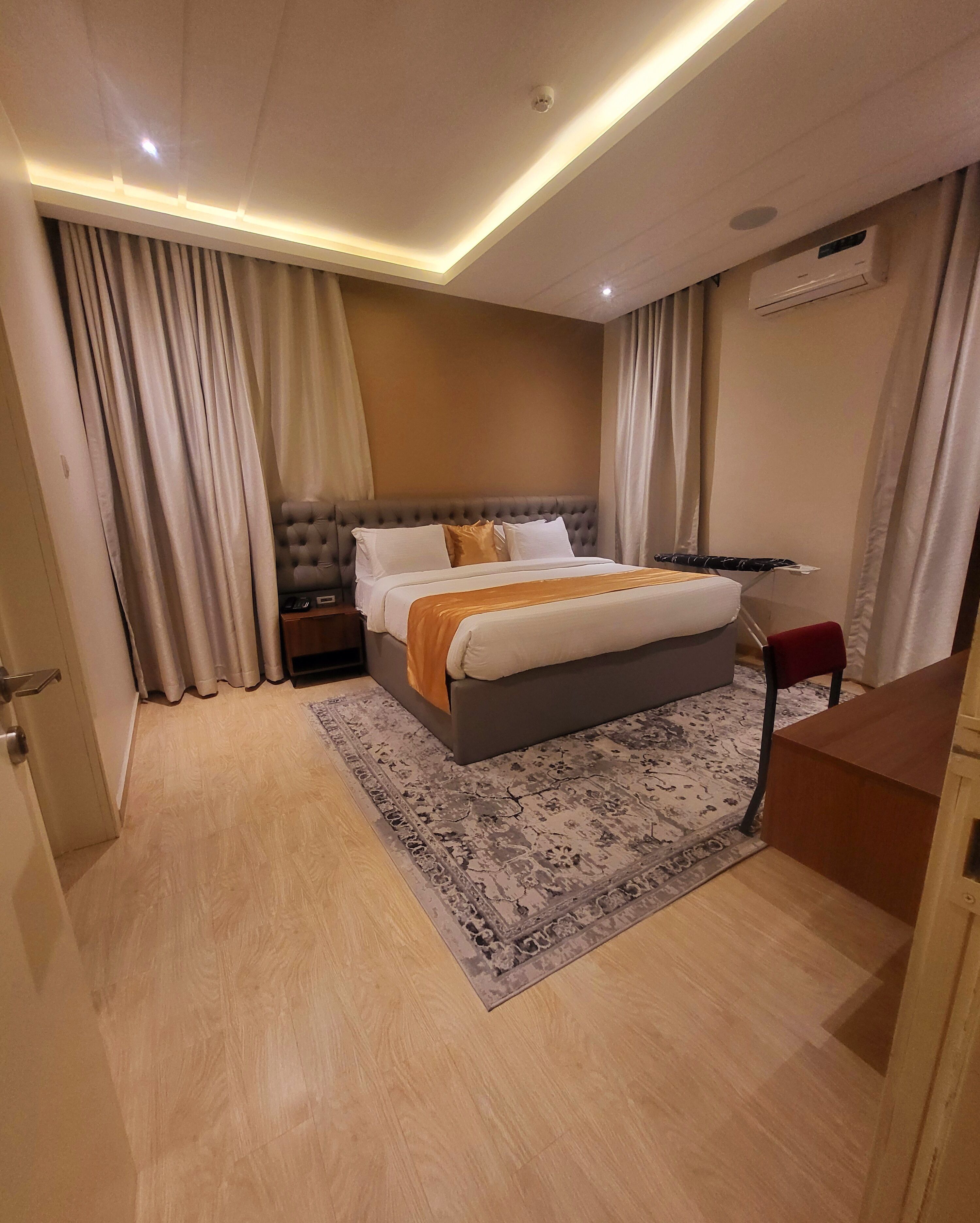 Habitación de hotel con cama, cortinas, tabla de planchar, escritorio y aire acondicionado.