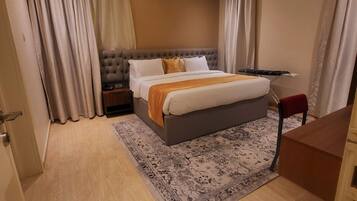 Habitación de hotel con cama, cortinas, tabla de planchar, escritorio y aire acondicionado.