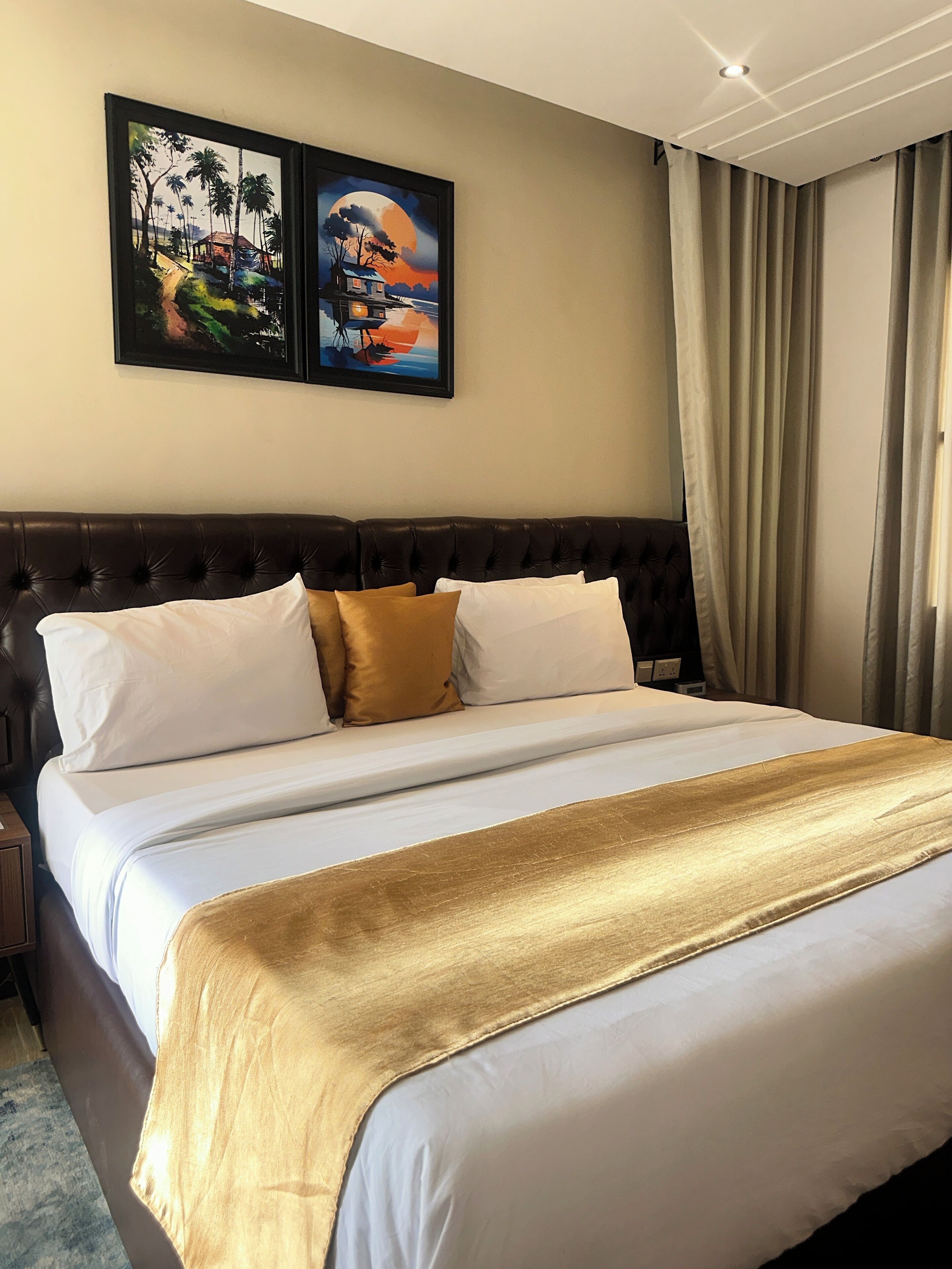 A hotel room with a large bed, a dark headboard, and two framed paintings on the wall.