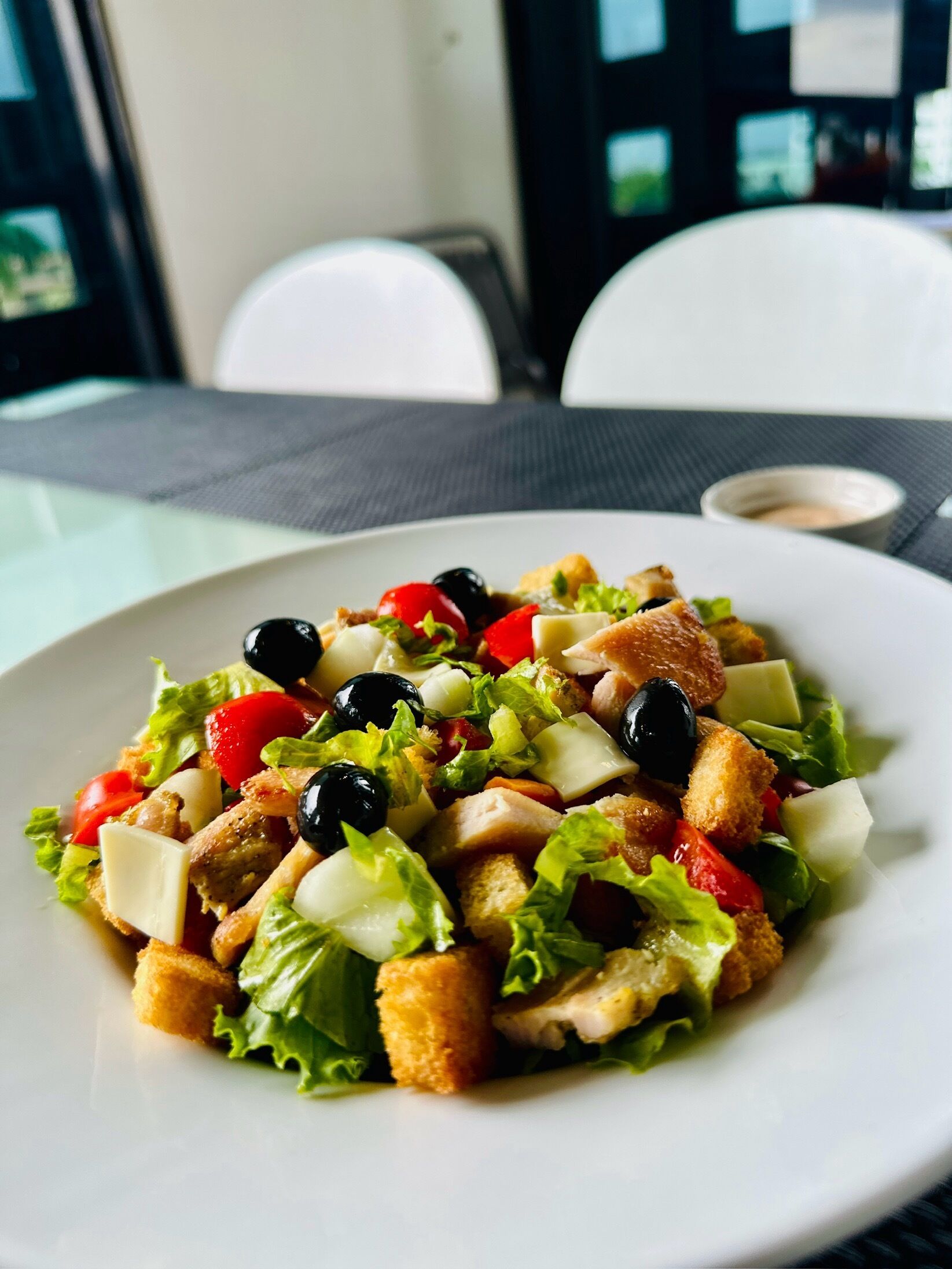 A plate of salad with croutons, cheese, and olives on a white plate.