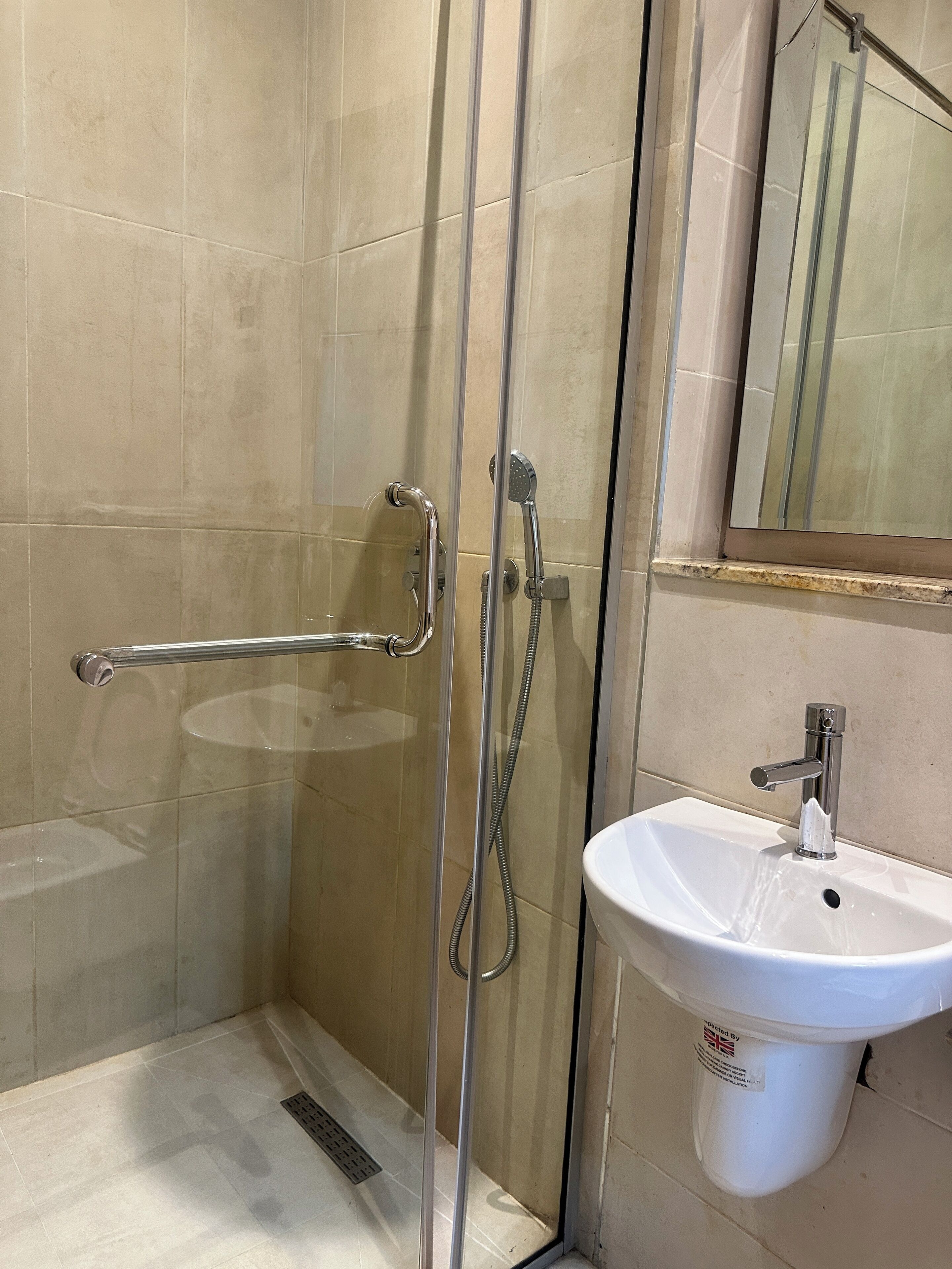 A glass-enclosed shower with a handheld showerhead and a handheld faucet.
