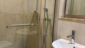 A glass-enclosed shower with a handheld showerhead and a handheld faucet.