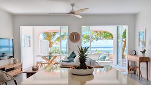 Ein modernes Wohnzimmer mit einem großen Glastisch, einem Deckenventilator und Meerblick durch große Fenster.