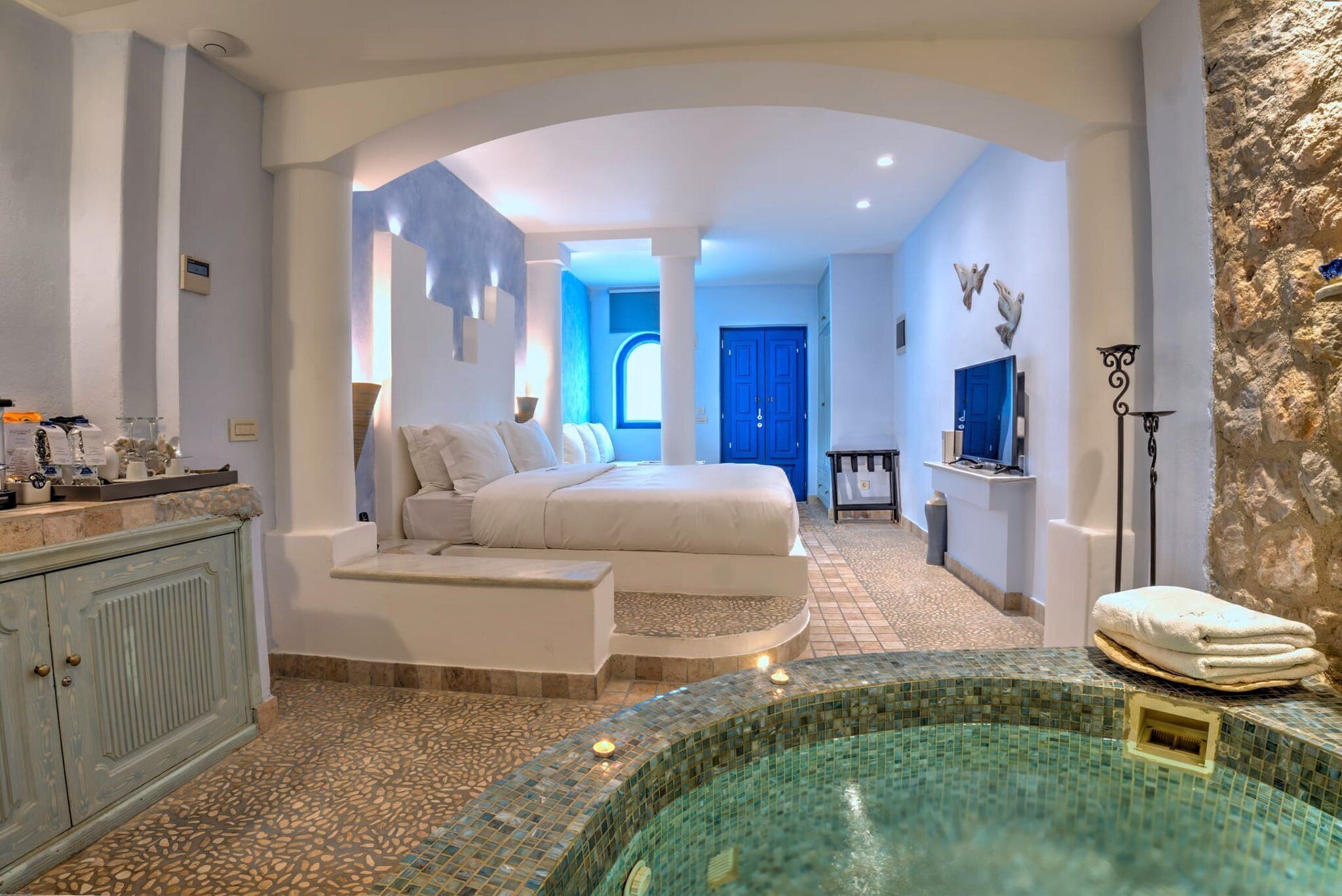 A spacious bedroom with a large bed, a built-in desk, and a glass-enclosed jacuzzi.