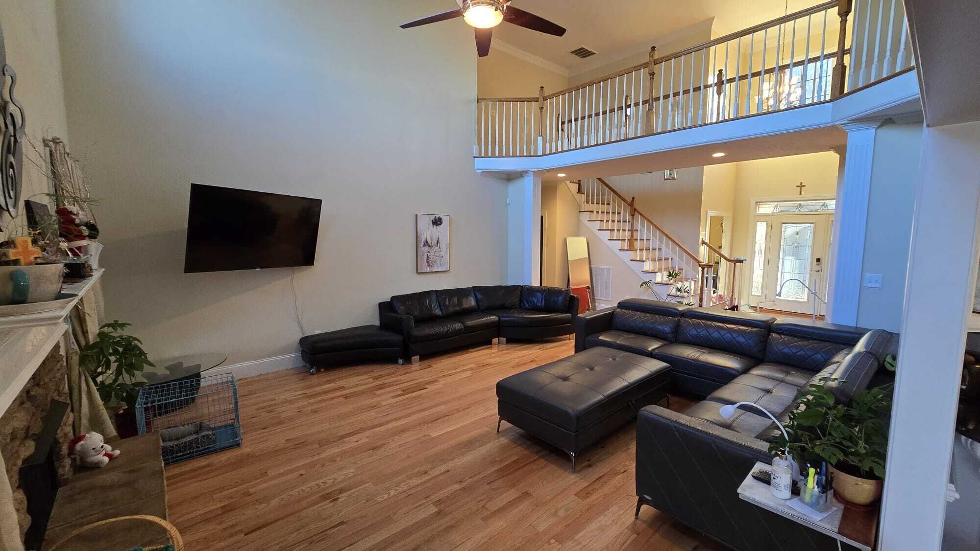A spacious living room with a large sectional sofa, a flat-screen TV, and a staircase leading to an upper level.