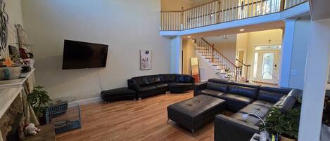 A spacious living room with a large sectional sofa, a flat-screen TV, and a staircase leading to an upper level.