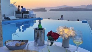 A dining area with a view of the sea, a pool, and a sunset. - Althene Suite, Divine Sea and Caldera Views,Furnished Balcony, Indoor Jacuzzi (Santorini)
