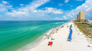 A beach with clear turquoise waters, a sandy shore, and a row of blue umbrellas. - Beachfront Balcony + Pool | Sleeps 3 | Pier Park (Panama City Beach)
