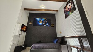 A modern bedroom with a dark brick wall, a large painting, a bed, and a TV. - Maisonnette Grande Hauteur Near Paris & Stade De France (Drancy)