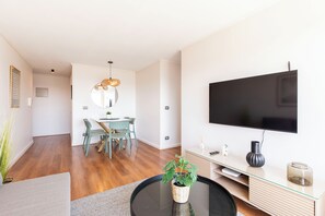 Una sala de estar moderna con comedor, un televisor de pantalla plana en la pared y una mesa de centro redonda con una planta.