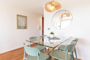 Un comedor moderno con una mesa de vidrio, sillas verdes, una planta en maceta y un espejo grande en la pared.