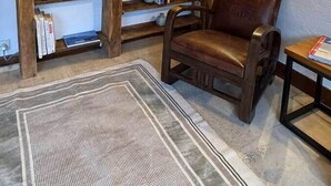 Ein gemütliches Wohnzimmer mit einem großen Flachbildfernseher, der an einer Holzwand befestigt ist, umgeben von Regalen mit Büchern und Dekoration. Ein Ledersessel und ein kleiner Tisch mit einer Zeitschrift sind ebenfalls zu sehen.