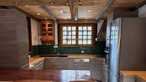 Eine Küche mit Kochinsel, Holzbalken, einer Wand aus Stein und einem großen Fenster.
