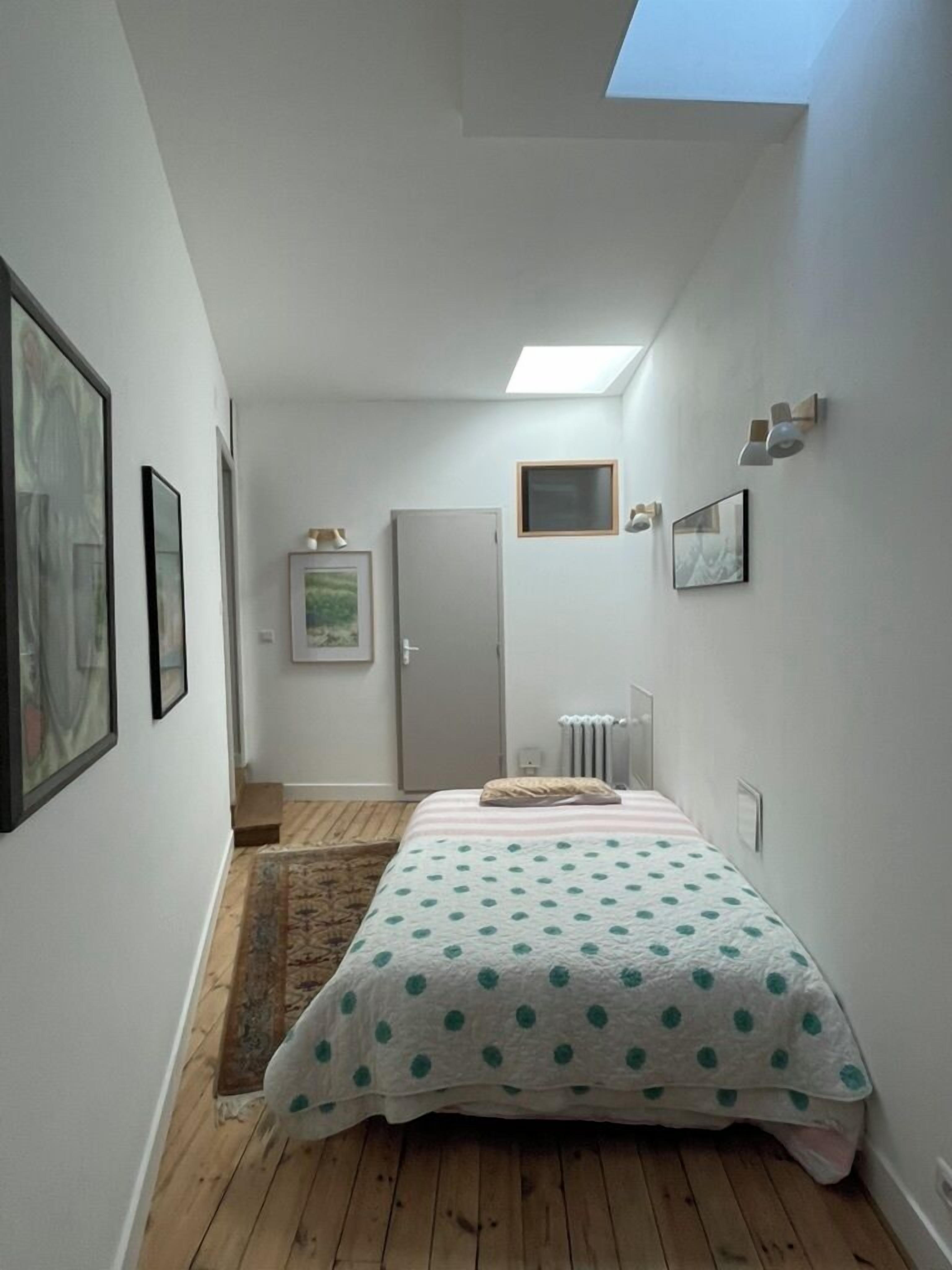 A narrow room with a bed, a radiator, a door, and a skylight.