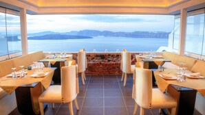 Un restaurant amb taules preparades per dinar, una paret de pedra i vista al mar.