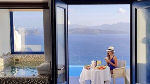 Habitació amb una porta gran oberta que dona a un balcó amb taula preparada per esmorzar i vista panoràmica de l'oceà.