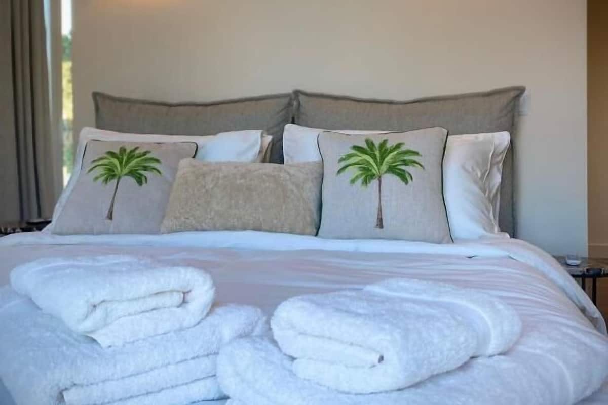Una cama bien hecha con sábanas blancas y dos almohadas, una con un diseño de palmera.