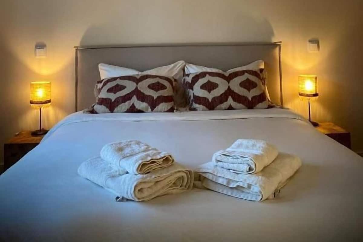 Una cama bien hecha con dos almohadas estampadas y toallas dobladas.