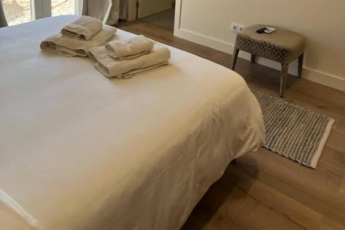 Habitación de hotel con cama, televisor de pantalla plana en la pared, un taburete pequeño y vistas al exterior mediante una puerta corrediza de vidrio.