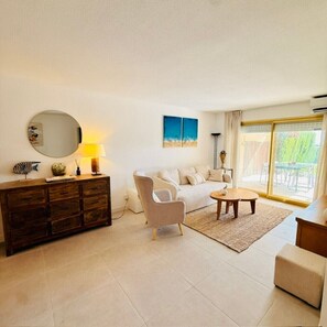 A living room with a sofa, armchair, coffee table, and a wooden cabinet. - 45.50 S'Agaró Montecarlo with private garden (Sant Feliu de Guixols)