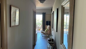 Ein Korridor mit Holzboden, gerahmten Kunstwerken an den Wänden und einer Sitzecke mit Stühlen und einem Tisch.
