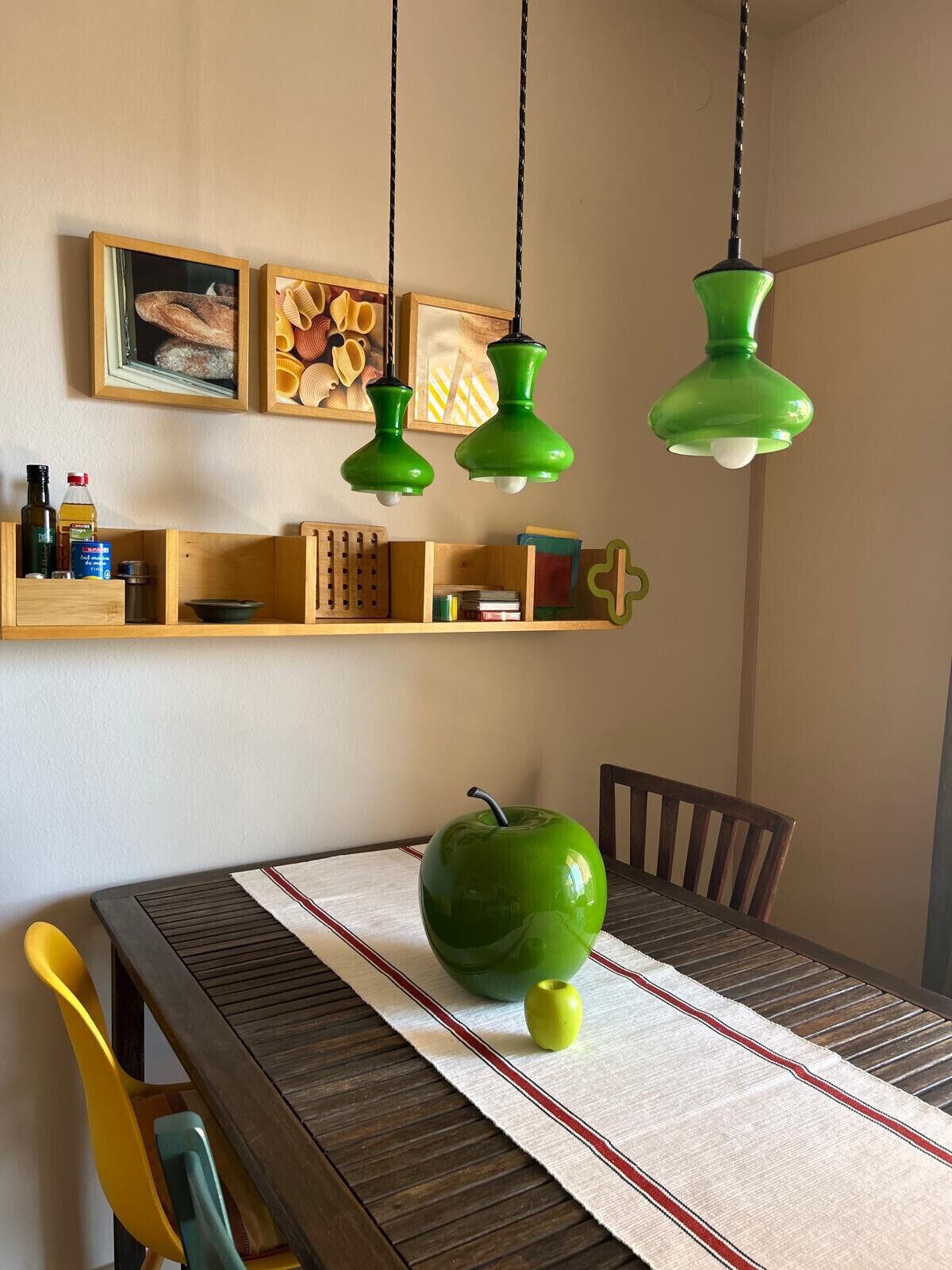 Un espace repas avec une table en bois, une pomme verte servant de décoration centrale et des lampes suspendues vertes.