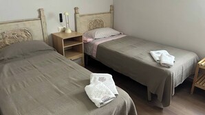 Ein Zimmer mit zwei Einzelbetten, einem Nachttisch, einer Lampe und einer Wandleuchte.