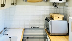 Ett kompakt kök med diskho, spis, mikrovågsugn och en varmvattenberedare som är monterad på väggen.