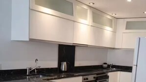 Een moderne keuken met witte kasten, een granieten werkblad, roestvrijstalen apparatuur en inbouwspots.