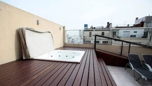Een dakterras met een houten terras, een jacuzzi en een zithoek met stoelen.