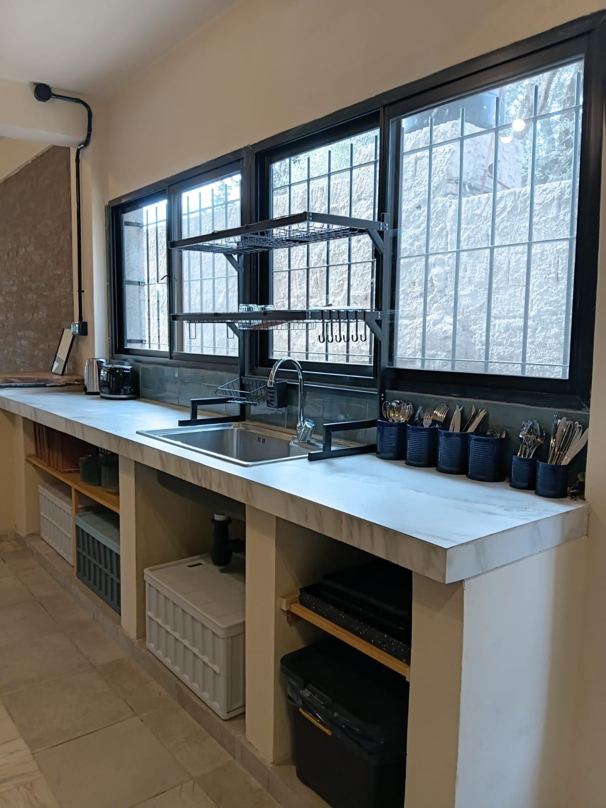 Una cocina con un ventanal grande, un lavamanos y un organizador para utensilios.
