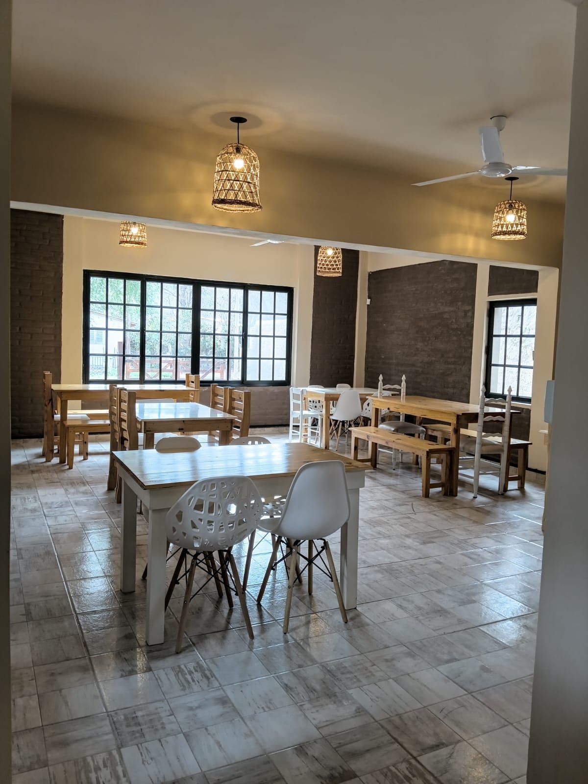 A spacious dining area with multiple tables and chairs, large windows, and ceiling fans.