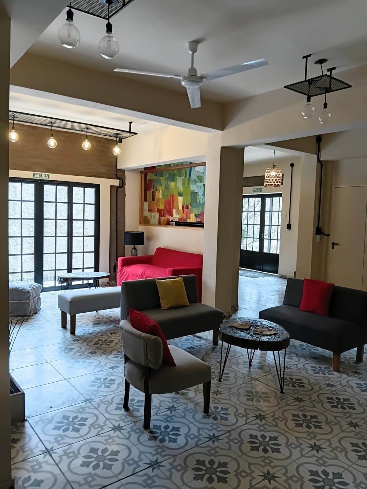 Amplia sala de estar con un sofá rojo, un sillón gris y una mesa de centro. Cuenta con varios ventiladores de techo e iluminación colgante.