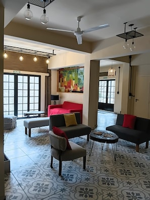 A spacious living area with a red sofa, a grey armchair, and a coffee table. There are multiple ceiling fans and pendant lights. - Hostel Waysanu (Capilla del Monte)