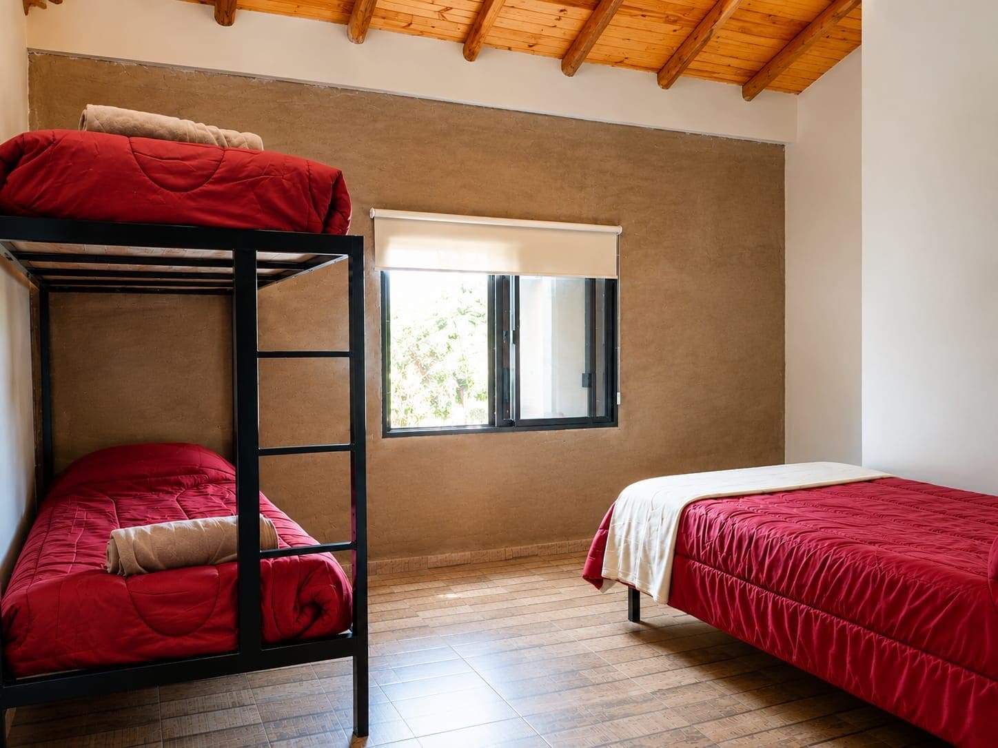 Quarto com cama de solteiro, beliche e janela com vista.